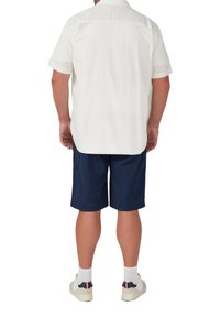 Kortekleurig wit overhemd met kraag, gecombineerd met marineblauwe shorts. Het overhemd heeft een gestructureerde stof; de schoenen zijn wit met blauwe en rode accenten.