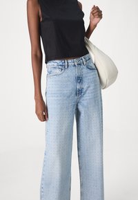 Jeans azzurri a gamba larga con un motivo a pois discreto, abbinati a un top nero aderente senza maniche e a una borsa a tracolla color crema.