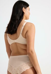 Bra beige con spalline morbide, design classico e chiusura con gancio. Slip abbinati presentano un bordo in pizzo lungo il margine inferiore. Tessuto dalla texture liscia.