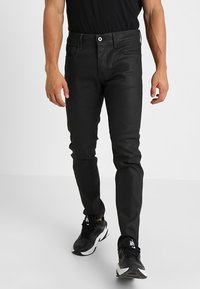 Svarta smala jeans med en jämn textur, femficksdesign och kontrasterande sömnadsdetaljer, tillsammans med svartvita sneakers.