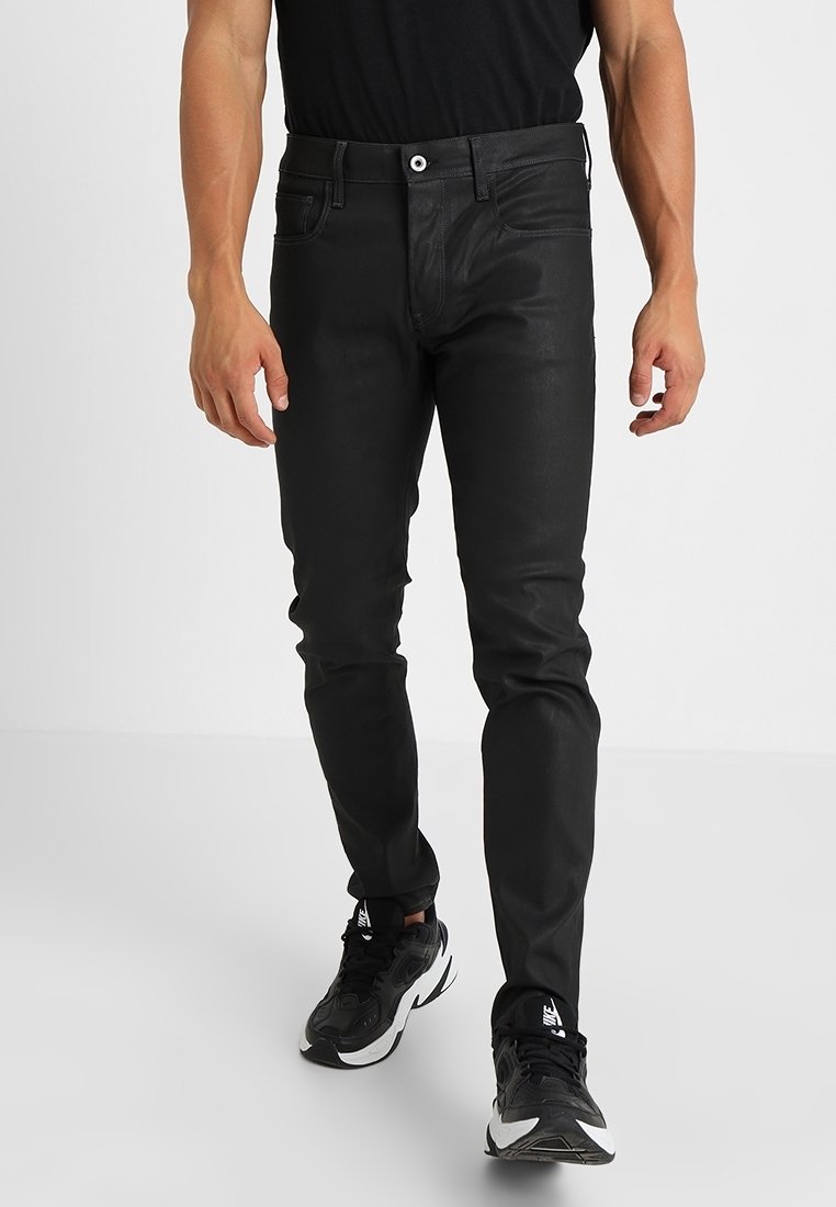 Svarta smala jeans med en jämn textur, femficksdesign och kontrasterande sömnadsdetaljer, tillsammans med svartvita sneakers.