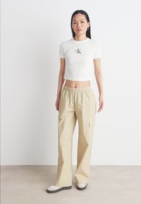 Witte cropped T-shirt met een zwart logo op de borst, gecombineerd met beige cargobroek met elastische taille en zijzakken in een relaxte pasvorm.