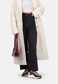Manteau en fausse fourrure crème, haut court blanc, pantalons wide-leg noirs à rayures, sac à main en vernis bourgogne, baskets imprimé léopard sur semelle blanche.