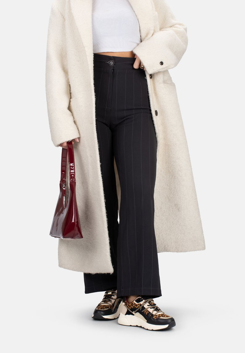 Manteau en fausse fourrure crème, haut court blanc, pantalons wide-leg noirs à rayures, sac à main en vernis bourgogne, baskets imprimé léopard sur semelle blanche.