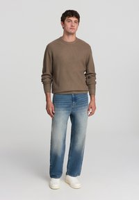 Maglione a coste marrone, jeans azzurri chiari con sfumatura in gradiente e sneakers bianche. Design semplice, vestibilità comoda e maniche lunghe.