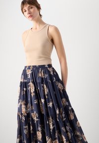 Beige tettskjorte i tank-top stil kombinert med en flytende, marineblå maxiskjørt med blomsterdesign i krem- og rustfarger, i et lagdelt design.