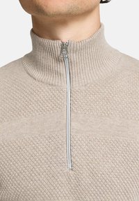 Beige Zip-Up-Pullover mit geripptem Kragen und strukturierter Oberfläche. Verfügt über einen halben Reißverschluss mit einem Metall-Ziehband. Aus weichem Strickstoff.