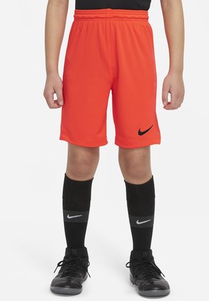 Pantaloni sportivi arancioni brillanti con una fascia elastica in vita e un logo Nike nero. Abbinati a calze nere fino al ginocchio con una striscia grigia.