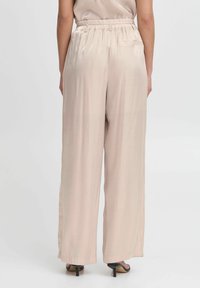 Lichtbeige wijde broeken met een gladde textuur, elastische tailleband en zijzakken, gecombineerd met zwarte haksandalen.