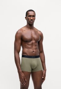 Grønne boksershorts med svart elastisk linning som har "HUGO" logo; tettsittende design, mykt stoff og kort benlengde.
