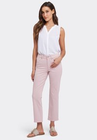 Jeans de tiro alto en rosa claro con un corte de pierna recta, combinados con una blusa sin mangas blanca y sandalias deslizantes de flores beige.