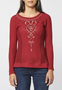 Haut rouge à manches longues en tissu texturé avec une broderie détaillée aux couleurs contrastantes. Coupe ajustée avec un col rond et un ourlet côtelé.