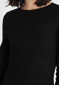 Czarna, prążkowana bluzka z długim rękawem, z okrągłym dekoltem, wykonana z teksturowanego materiału elastycznego, zapewniającego dopasowany krój.