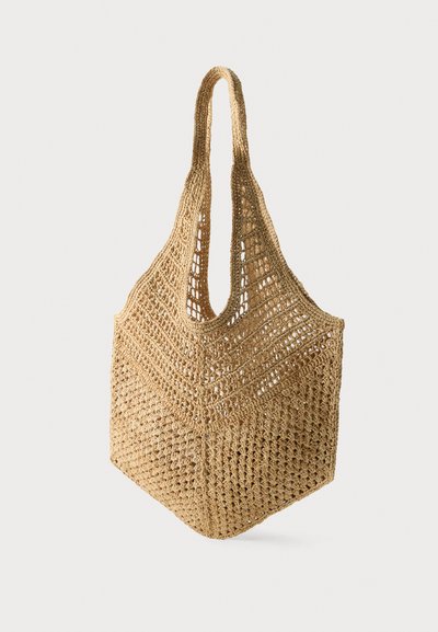 Sac cabas de marché beige en crochet tissé à la main avec de larges anses et un motif ajouré et aéré.
