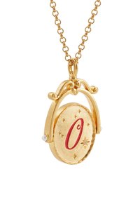 Kuldne ripatsidega kaelakee, millel on ümmargune ripats, millel on punane "O" ja väikesed täheaktsendid, riputatud delikaatse kuldse ahela külge.
