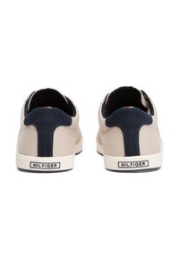 Beige plátěné tenisky s námořnicky modrými akcenty na patě a bílou podrážkou. Mají prošívaný design a značkové logo na patě.
