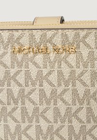 Borsa Michael Kors in tono oro con tessuto testurizzato caratterizzato da un motivo geometrico. Presente una maniglia superiore e una chiusura con zip.