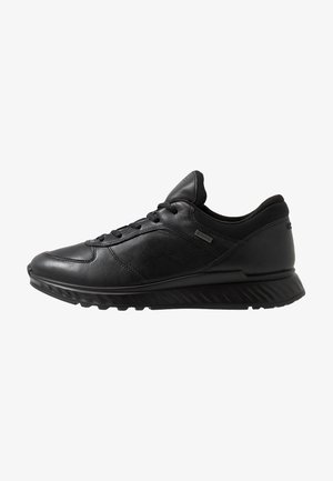 Schwarze Sportschuhe aus Leder und Mesh, mit abgerundetem Zehenbereich, Schnürverschluss und strukturiertem Sohlen mit Profilrillen.