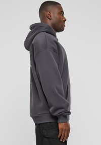 Mørkegrå hettegenser med en avslappet passform, stor hette, frontlomme og ribbede mansjetter. Myk tekstur med minimalistiske designdetaljer.