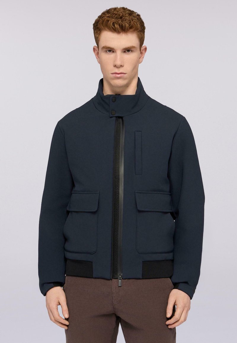 Giacca blu navy con colletto alto, chiusura con zip, due tasche frontali e un pannello testurizzato lungo la zip. Il tessuto sembra liscio.