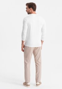 Weißes Langarmhemd mit Rundhalsausschnitt, kombiniert mit hellbeigen Hosen und Sneakers. Glatter Stoff mit lässiger Passform.