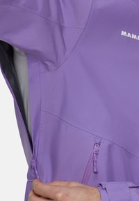 Lila lättviktsjacka med en zip-försedd ficka och strukturerad tyg. Designen är elegant med en åtsittande silhuett och justerbara ärmslut.