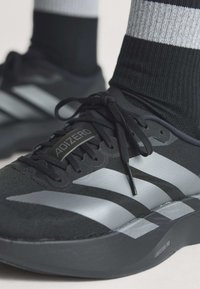 Μαύρα και γκρι παπούτσια τρεξίματος Adidas Adizero με μαύρα κορδόνια και μαύρες και γκρι ριγέ κάλτσες.