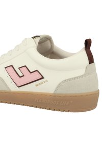 White sneaker with a pink logo, beige suede accents, and brown heel tab. Features a textured rubber sole with branding.