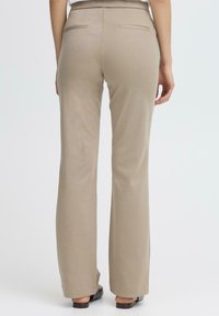 Pantaloni beige a palazzo con una texture liscia, dotati di due tasche posteriori e una vita a media altezza, abbinati a sandali piatti.