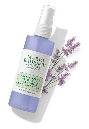 Gesichtssprühflasche mit den Aufdrucken Aloe, Kamille und Lavendel neben Lavendelzweigen auf weißem Hintergrund.
