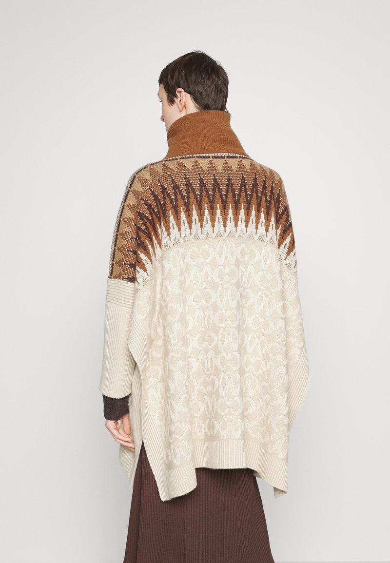 Strickponcho mit hohem Kragen, der ein geometrisches Design in Braun und Creme aufweist sowie gerippte Kanten. Weiche Textur, oversized Passform und Schlitze an den Seiten.