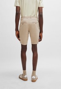 Shorts de algodón beige con cinturilla, dos bolsillos traseros y dobladillo. Combinados con calcetines claros y zapatillas beige.