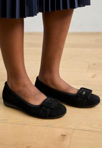 Ballerine nere in suede con punta arrotondata, dotate di una fibbia decorativa sulla parte superiore. Il design include una suola imbottita per il comfort.
