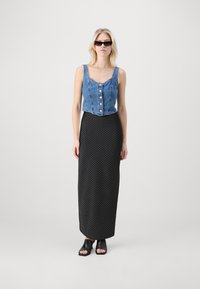 Top court en denim avec des boutons, associé à une jupe maxi noire à pois. Le modèle porte des chaussures ouvertes noires et des lunettes de soleil.