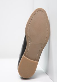 Czarne skórzane buty z gładką cholewką i jasnobrązową gumową podeszwą. Podeszwa ma teksturowany wzór dla lepszej przyczepności.