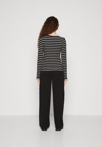 Svart långärmad randig topp med vita horisontella ränder, i kombination med lösa svarta byxor som har sidofickor och rak bendesign.