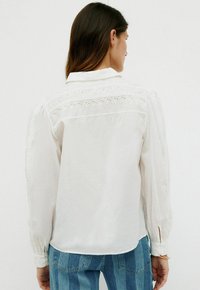 Hvid langærmet skjorte lavet af letvægtsstof, med en detaljeret broderet yoke og knapmanchetter, parret med blå stribede jeans.