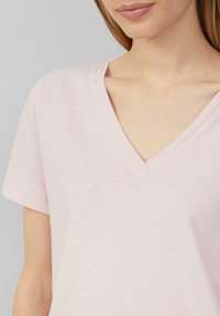 Lichtroze V-hals t-shirt met korte mouwen. Zachte textuur, subtiel heatherpatroon en versterkte stiksels rond de halslijn.