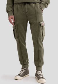 Pantaloni cargo verde oliva in morbido cotone misto, con tasche laterali, polsini elasticizzati e cuciture visibili per un tocco di dettaglio.