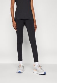 Sorte idrettsleggings med slim fit og glatt tekstur, kombinert med lysegrå joggesko med blå og oransje detaljer.