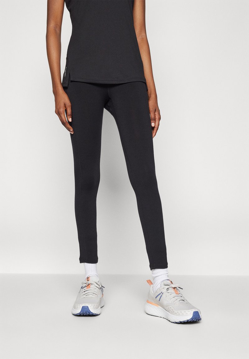 Sorte idrettsleggings med slim fit og glatt tekstur, kombinert med lysegrå joggesko med blå og oransje detaljer.