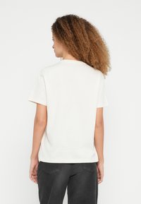 Κρεμ κοντομάνικη μπλούζα με στρογ�γυλή λαιμόκοψη, κατασκευασμένη από βαμβάκι. Το ύφασμα φαίνεται απαλό με ομαλή υφή.