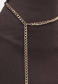 Mørkebrun ribbet stof med en gylden kædeaccent fastgjort i taljen, der har en glat tekstur og skinnende metalled.