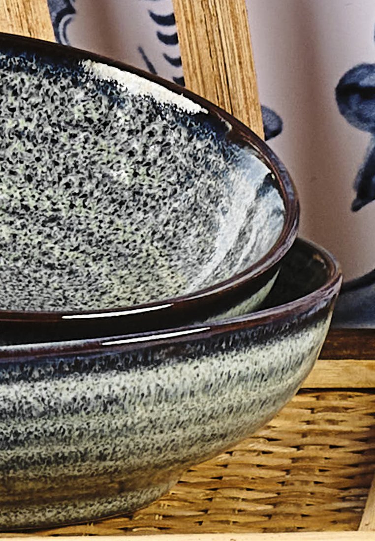 Cuencos de cerámica de diferentes tamaños, con un esmalte moteado en gris y azul, de textura suave y un borde oscuro, colocados en una cesta tejida.