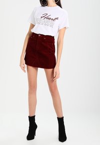 Vitt t-shirt med texten "Heartbreaker", kombinerat med en röd kordflort mini kjol. Svarta ankellånga stövlar avslutar outfiten.