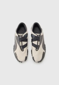 Pair of beige and gray Puma sneakers with black crisscross straps and textured soles on a white background.
