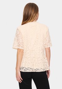 Peach lace blouse with short sleeves, floral patterns, peplum hem, and a scalloped lace edge. Textured, soft fabric.