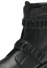 Black leather ankle boots feature a smooth texture, decorative black rectangular studs, and a stylish strap accenting the upper.