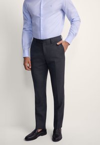 Ciemnoszare, dopasowane spodnie wykonane z gładkiej tkaniny, zestawione z jasnoniebieską koszulą na guziki i czarnymi eleganckimi butami.