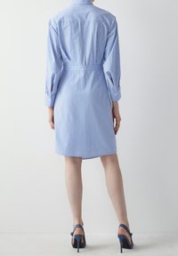 Abito camicia a righe blu e bianche con maniche lunghe, una cintura legata in vita e una vestibilità dritta, abbinato a sandali blu con tacco alto.